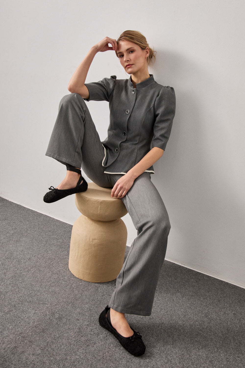 Chaqueta entallada en color gris con vuelo y pinzas en pecho. Tiene hombros rizados, manga corta, cuello mao y detalle a contraste en bajo.